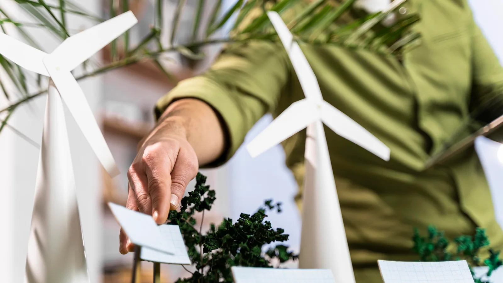 Person arranging miniature wind turbines and solar panels in a renewable energy project model